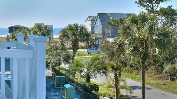 A coastal property with a view of the sea, a large house with a balcony, and a parking area with a car. - Explore Oak Island from OW 6204-Anchors Away, a 3BR oceanview condo for 8. (Oak Island)