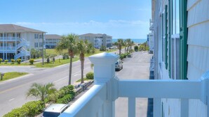 Un hotel frente a la playa con edificios de varios pisos, una calle con coches aparcados y palmeras.