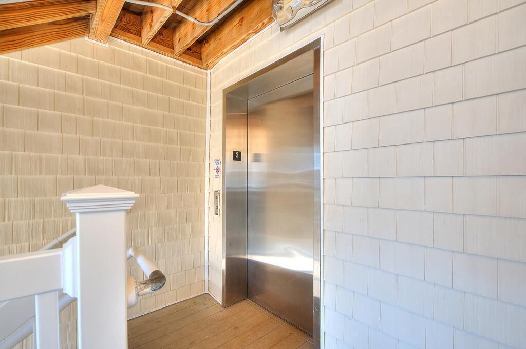 A modern elevator with a metallic finish, white tiled walls, and a wooden ceiling.