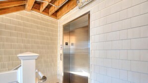 Un ascensor moderno con detalles metálicos, paredes de azulejos blancos y techo de madera.