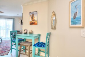 A dining area with teal chairs and a table, a framed picture of a bird, and a wall-mounted mirror.