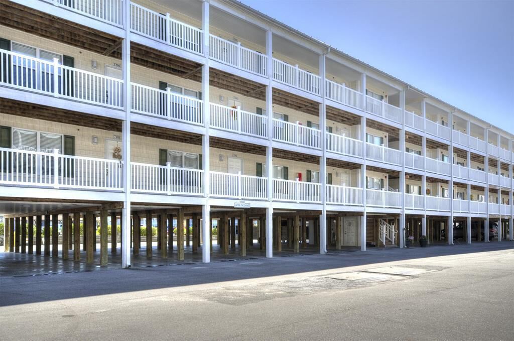 A multi-story hotel with balconies, a covered parking area, and a clear sky.