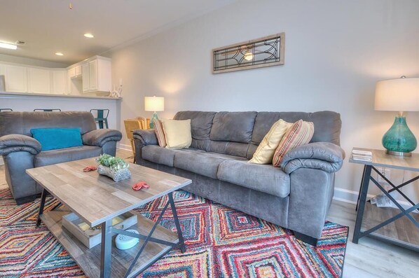 A modern living room with a grey sofa, a wooden coffee table, and a colorful rug.