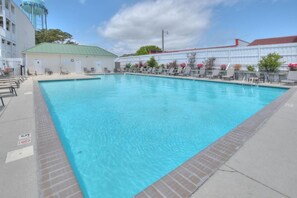 A rectangular swimming pool with a tiled edge, surrounded by lounge chairs and a covered area with a red roof.