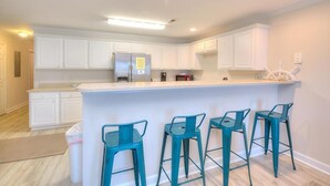 Una cocina moderna con armarios blancos, un refrigerador de acero inoxidable, una cafetera y una barra con cuatro taburetes color turquesa.