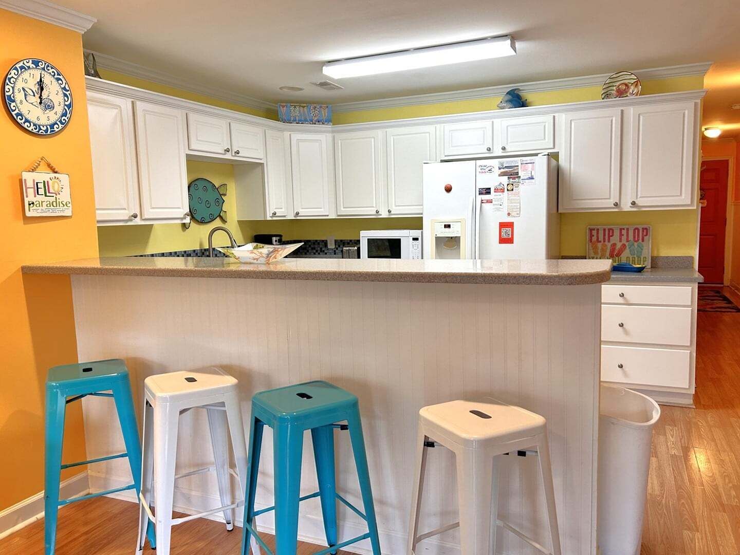 Una cucina con mobili bianchi, un forno a microonde, un frigorifero e tre sgabelli blu.