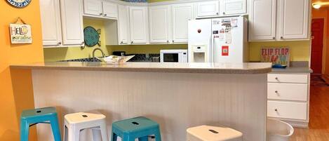 Una cucina con mobili bianchi, un forno a microonde, un frigorifero e tre sgabelli blu.
