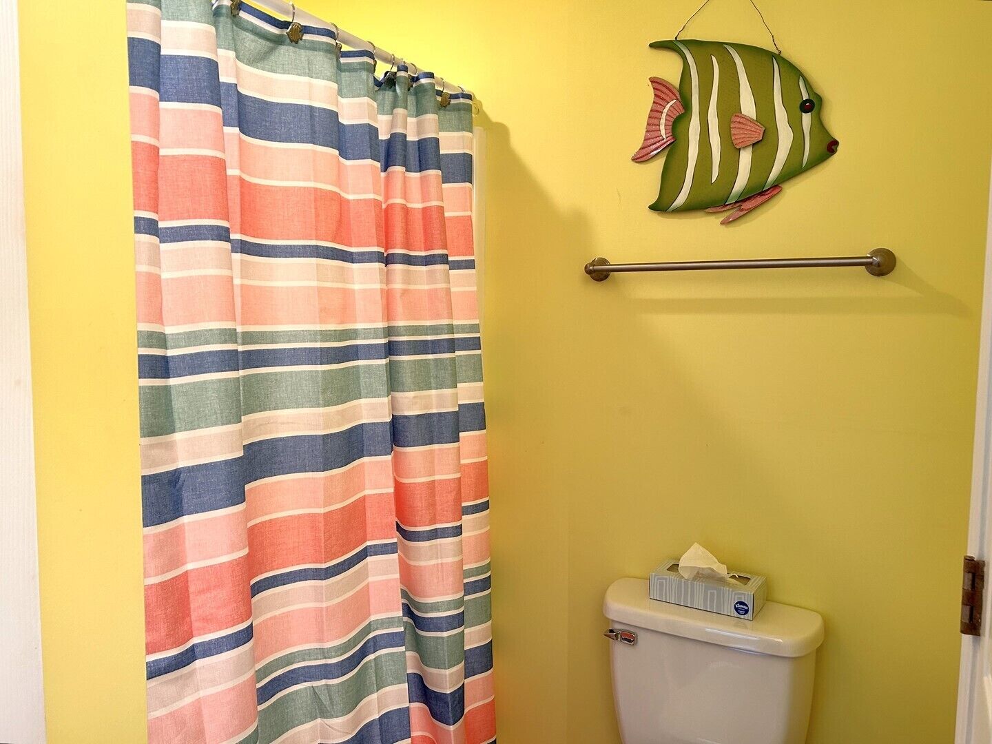 A bathroom with a striped shower curtain, a toilet, and a towel rack with a towel.