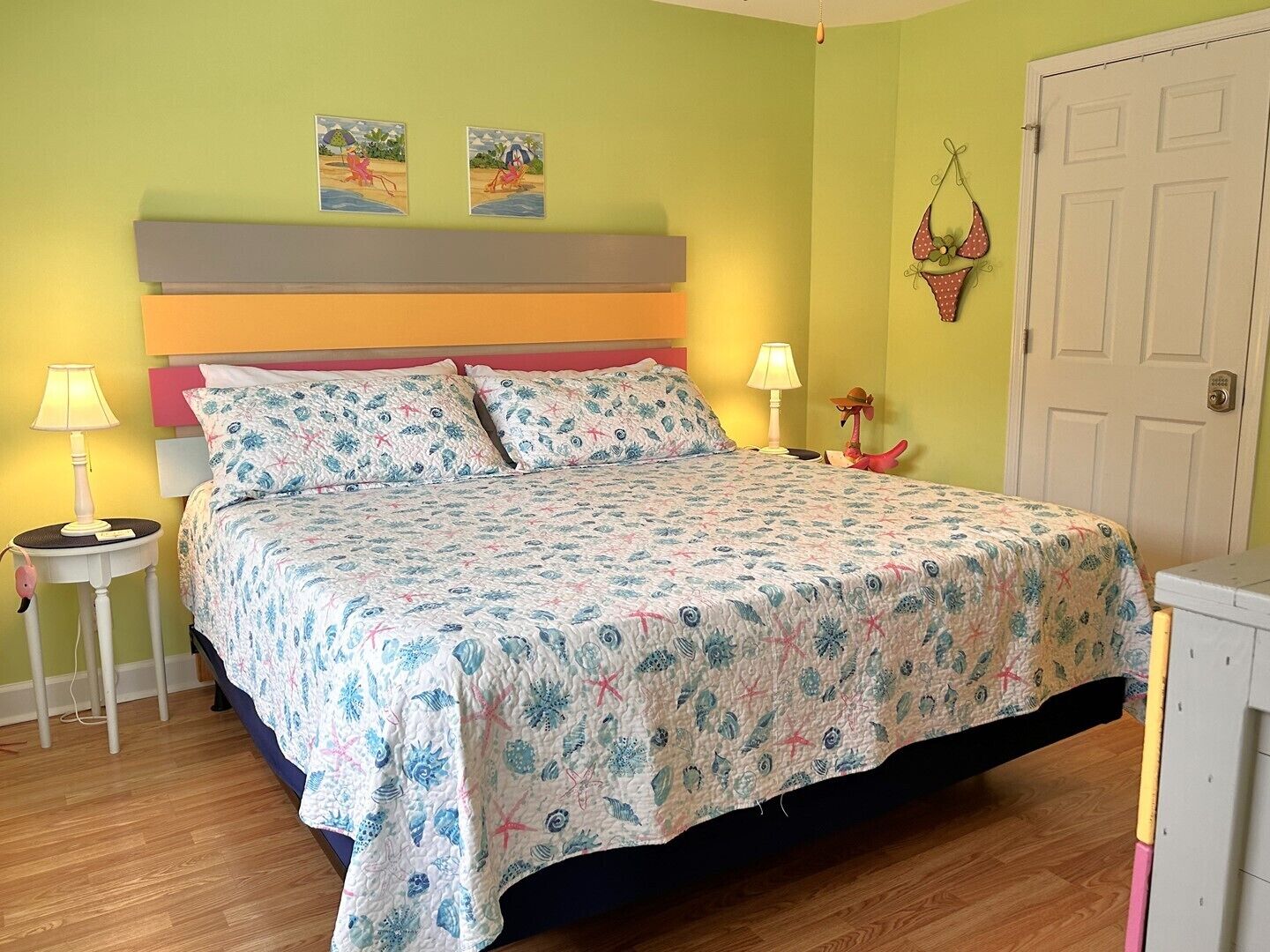 A bedroom with a bed, two bedside lamps, a nightstand, a door, and two wall art pieces.