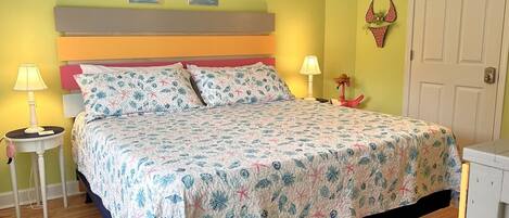 Une chambre à coucher comprenant un lit, deux lampes de chevet, une table de chevet, une porte et deux œuvres d’art mural.