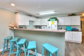 Una cocina con armarios blancos, una isla central con taburetes y un refrigerador con un letrero verde.