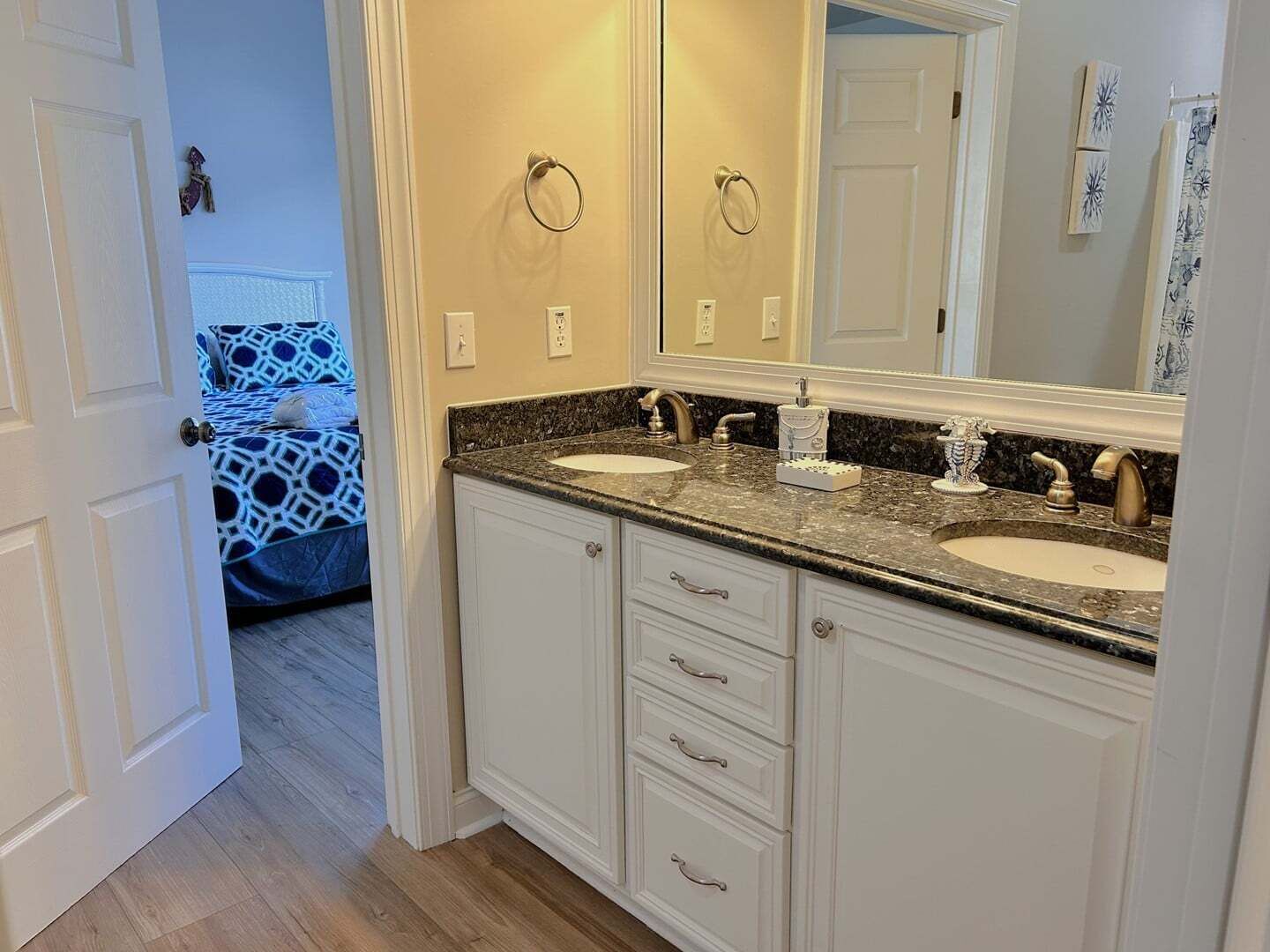 Une salle de bain avec deux lavabos, un grand miroir et une porte donnant sur une chambre.