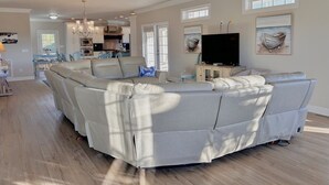 A spacious living room with a sectional sofa, a ceiling fan, and artwork on the walls.
