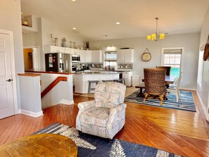 A spacious living area with a patterned armchair, a wooden coffee table, and a dining area with a wicker chair. - Experience oceanfront luxury at Pirate's View in Oak Island—perfect for 16 guests! (Oak Island)