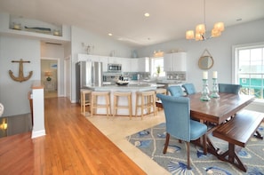A spacious kitchen with a central island, wooden bar stools, and a dining table with blue chairs.