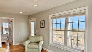 A room with a large window, a chair, a table, and a door leading to a hallway. - Experience oceanfront luxury at Pirate's View in Oak Island—perfect for 16 guests! (Oak Island)
