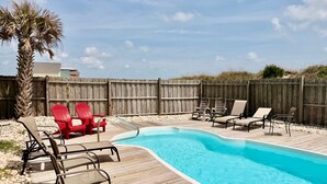 A wooden deck with a swimming pool, surrounded by a wooden fence, and includes red and beige lounge chairs. - Experience oceanfront luxury at Pirate's View in Oak Island—perfect for 16 guests! (Oak Island)