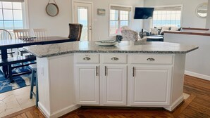 A kitchen with a granite countertop, white cabinetry, and a dining area with a table and chairs. - Experience oceanfront luxury at Pirate's View in Oak Island—perfect for 16 guests! (Oak Island)