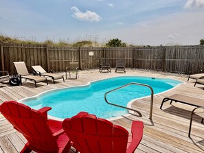 A swimming pool with a wooden deck, surrounded by lounge chairs and red Adirondack chairs. - Experience oceanfront luxury at Pirate's View in Oak Island—perfect for 16 guests! (Oak Island)