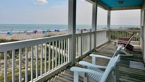 A covered deck with a view of the beach, white railings, and wooden flooring. - Experience oceanfront luxury at Pirate's View in Oak Island—perfect for 16 guests! (Oak Island)
