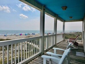 Eine überdachte Terrasse mit Blick auf den Strand, weiße Geländer und Holzboden.