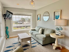 A living room with a sofa, a coffee table, a lamp, and a view of a balcony. - Experience oceanfront luxury at Pirate's View in Oak Island—perfect for 16 guests! (Oak Island)