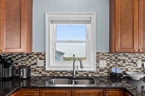 A kitchen with a large window, a stainless steel sink, and a tiled backsplash.
