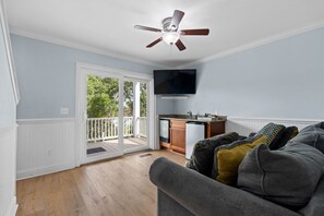 A living room with a gray couch, a ceiling fan, and a view of a balcony.
