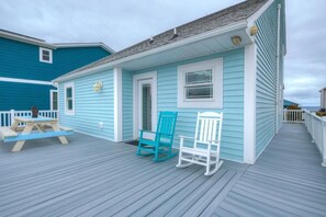 A light blue house with a porch, two rocking chairs, and a picnic table. - Discover ocean views at Salt Shack, Oak Island! Perfect for families and pets, sleeps 8. (Oak Island)