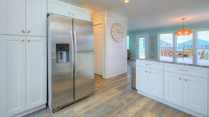 A modern kitchen with white cabinetry, a stainless steel refrigerator, and a built-in water dispenser. - Discover ocean views at Salt Shack, Oak Island! Perfect for families and pets, sleeps 8. (Oak Island)