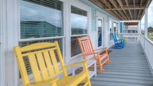 A covered porch with colorful Adirondack chairs and a wooden deck. - Discover ocean views at Salt Shack, Oak Island! Perfect for families and pets, sleeps 8. (Oak Island)