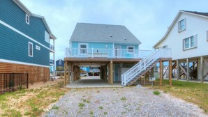 A two-story building with a covered entrance and a staircase leading to an upper deck. - Discover ocean views at Salt Shack, Oak Island! Perfect for families and pets, sleeps 8. (Oak Island)
