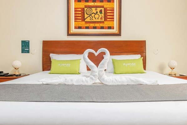 Restful retreat with a heart-shaped towel arrangement and plush pillows, featuring a framed artwork above the bed.