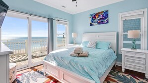 Un dormitorio con una cama grande, un ventilador de techo, un cuadro y vistas al océano.