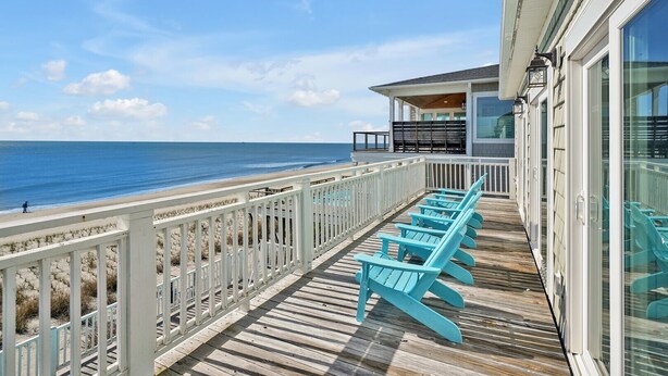 Una terraza de madera con sillas Adirondack turquesas con vista a una playa.
