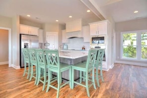 A spacious kitchen with white cabinets, a central island, and four green chairs.