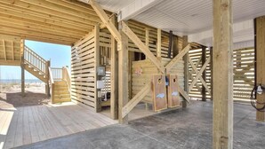 Een houten chalet met een trap naar een terras, een grote houten deur en uitzicht op het strand.