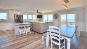 Een ruime keuken met een groot eiland, barstoelen, een eettafel met stoelen en uitzicht door de ramen.