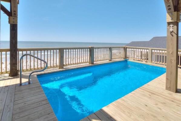 A wooden deck with a swimming pool, wooden railings, and a view of the ocean.