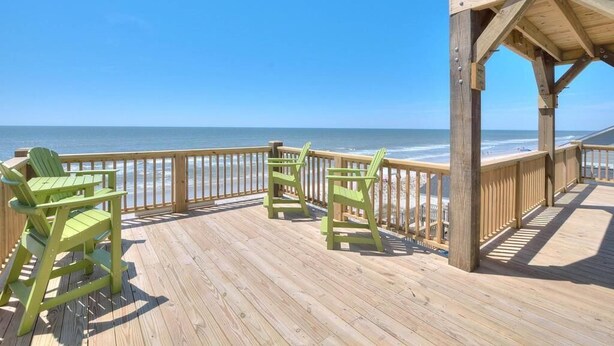 Een houten terras met uitzicht op de oceaan, met twee groene Adirondack-stoelen.