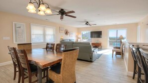 A spacious living area with a dining table, chairs, a sofa, and a balcony with a view. - Seas the Moment: 5BR oceanview retreat in Oak Island, perfect for families! (Oak Island)