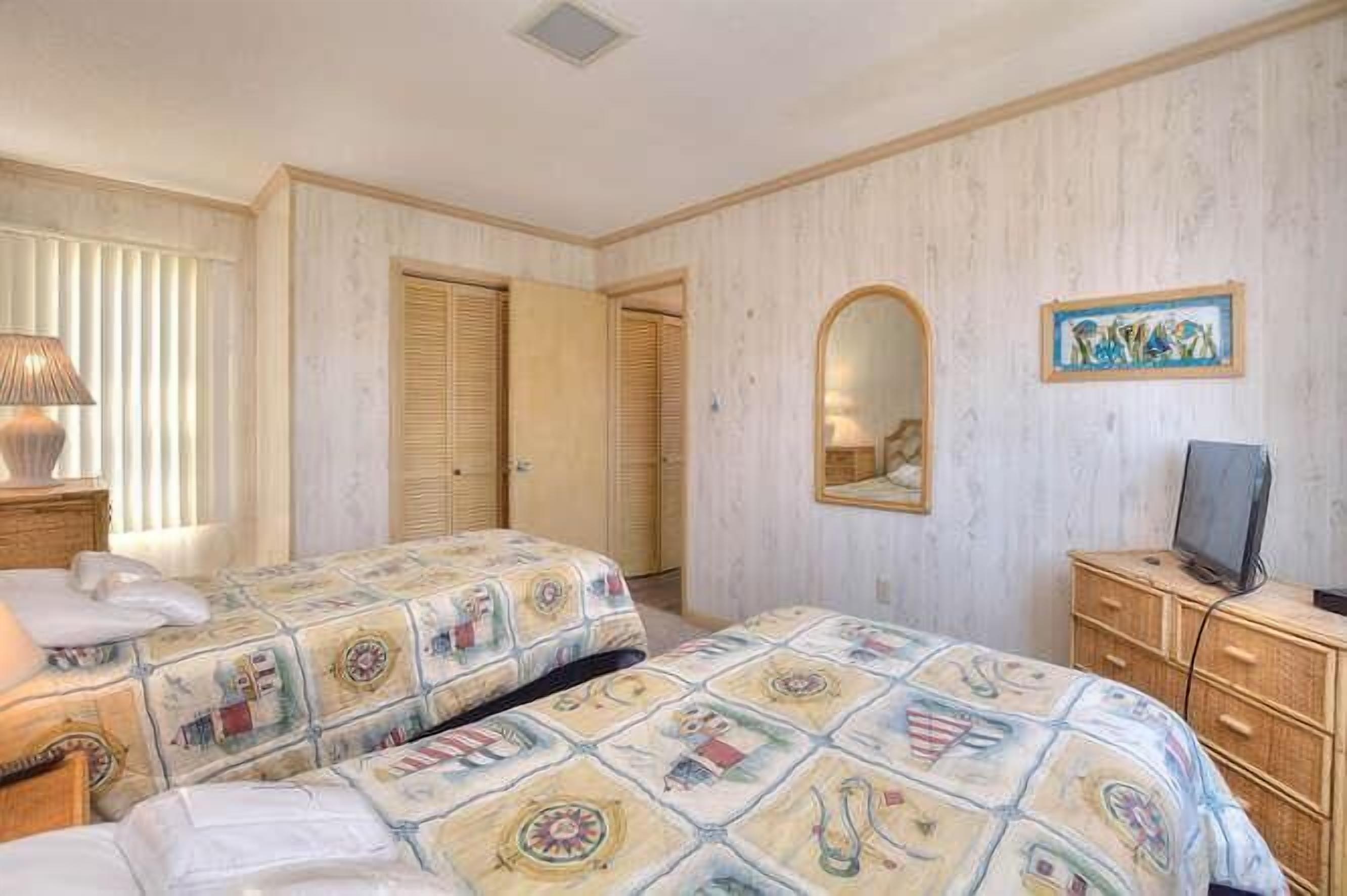 Une chambre d’hôtel avec deux lits, une commode, une télévision et un miroir.