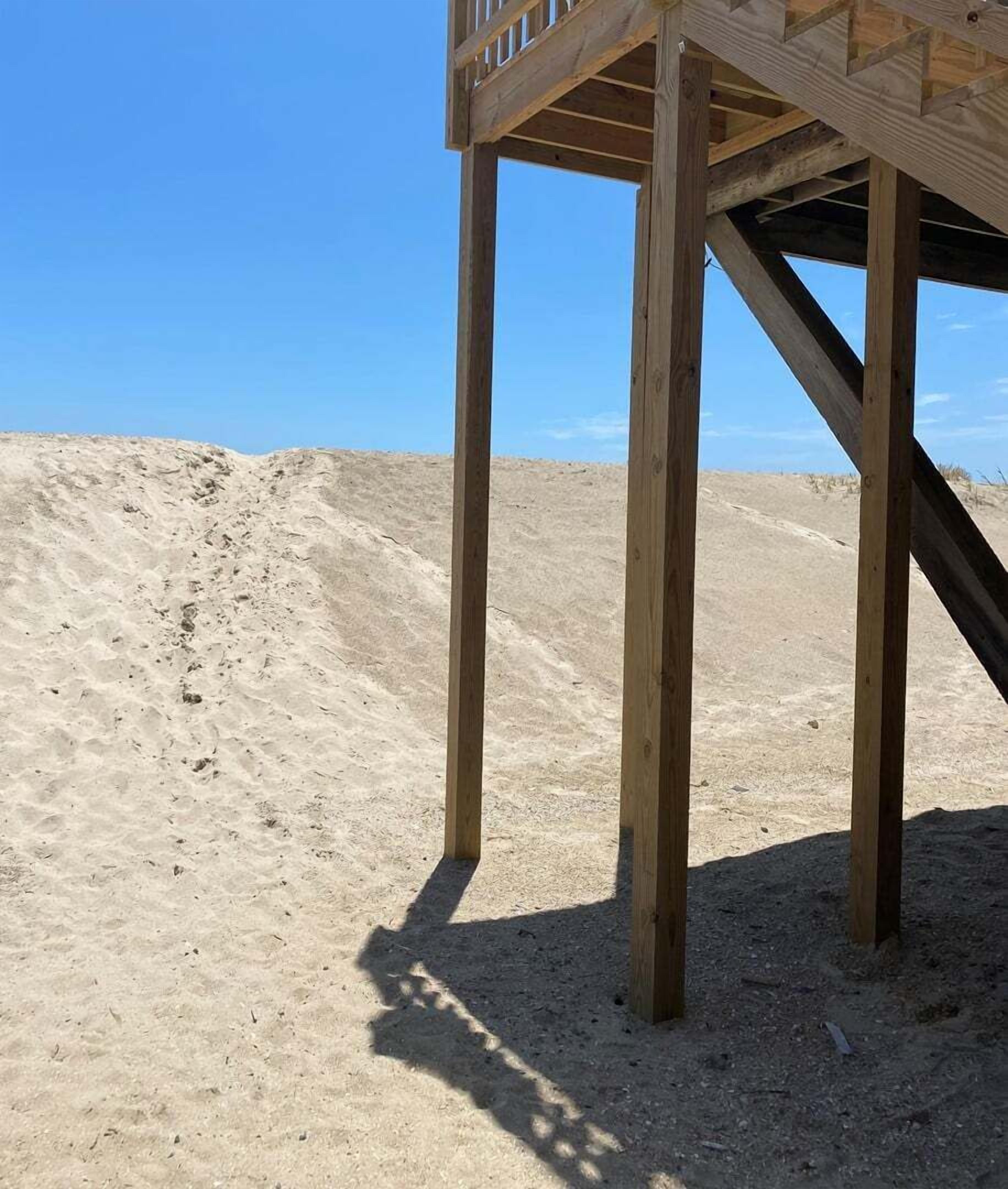 A wooden structure with a staircase leading up to a platform, surrounded by sand dunes.