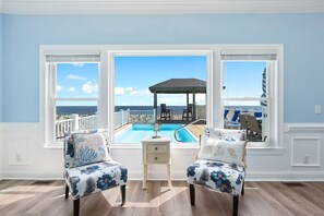 A room with a view of a pool and a gazebo, two chairs with floral upholstery, and a small white table.