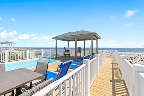 A wooden deck with a pool, lounge chairs, and a gazebo overlooking the beach.