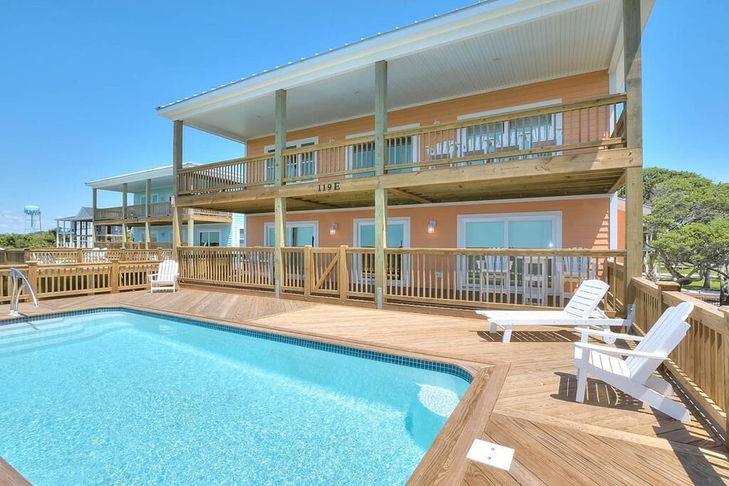 A two-story building with a pool and deck chairs.
