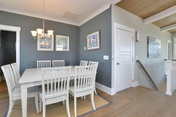 A dining area with a white table and chairs, a chandelier, framed pictures on the wall, and a white door.