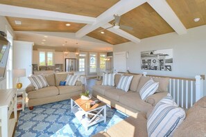 A spacious living room with a large sofa set, a coffee table, and a dining area with a kitchen in the background.