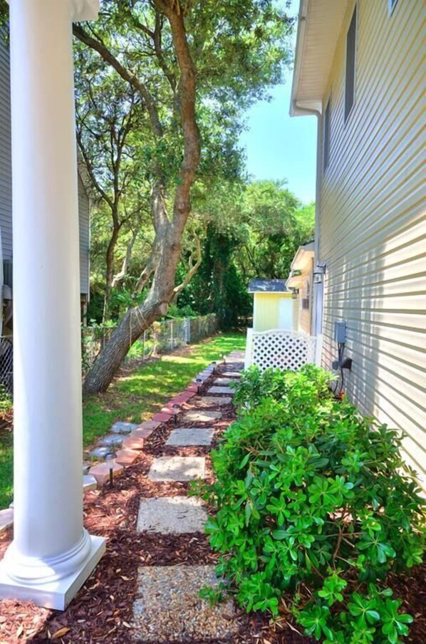 A pathway leading to a house with a white column, surrounded by greenery and a fence.