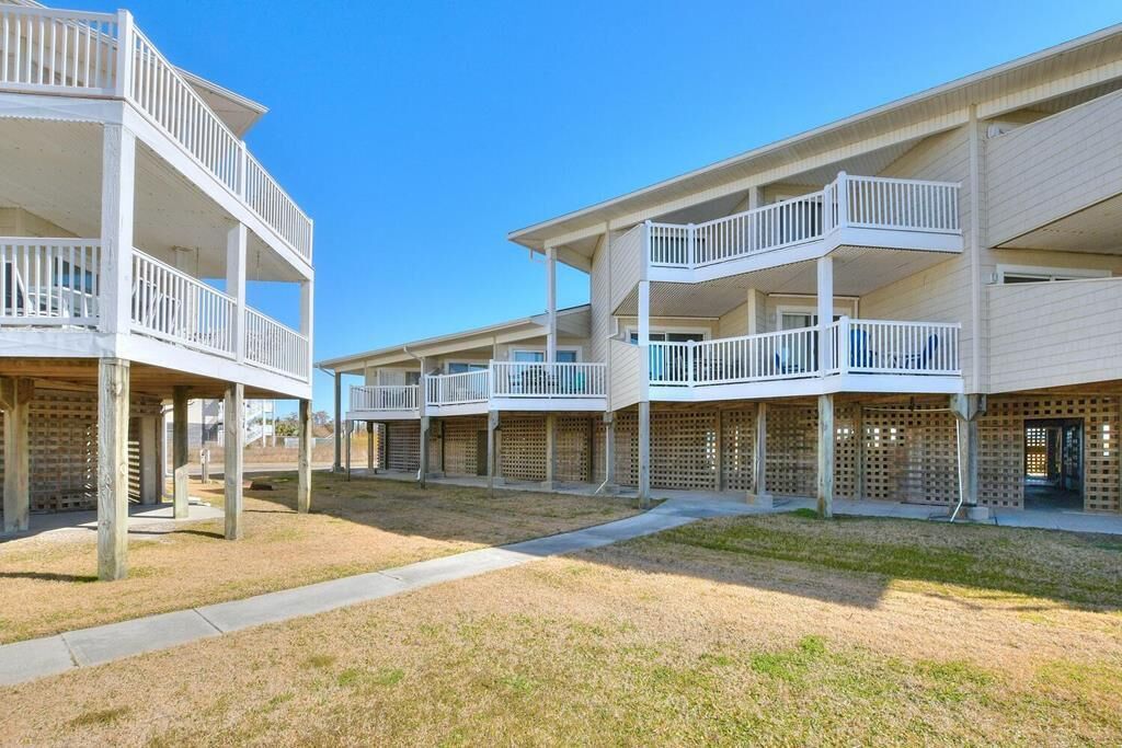 Un hilero de bungalows frente a la playa, con balcones, un paseo techado y una zona verde.